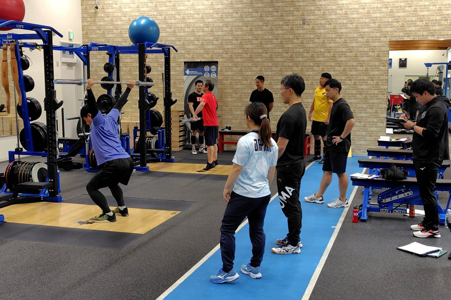 ウエイトリフティングをする男性を見ている人たち