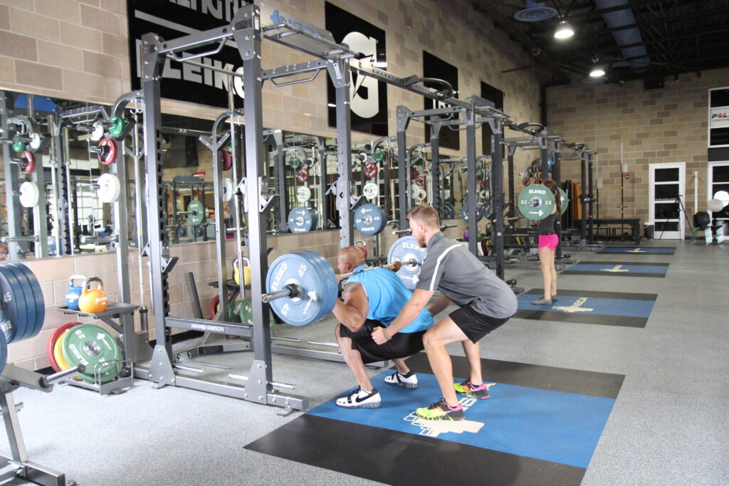 トレーナーとバーベルでトレーニングをしている人